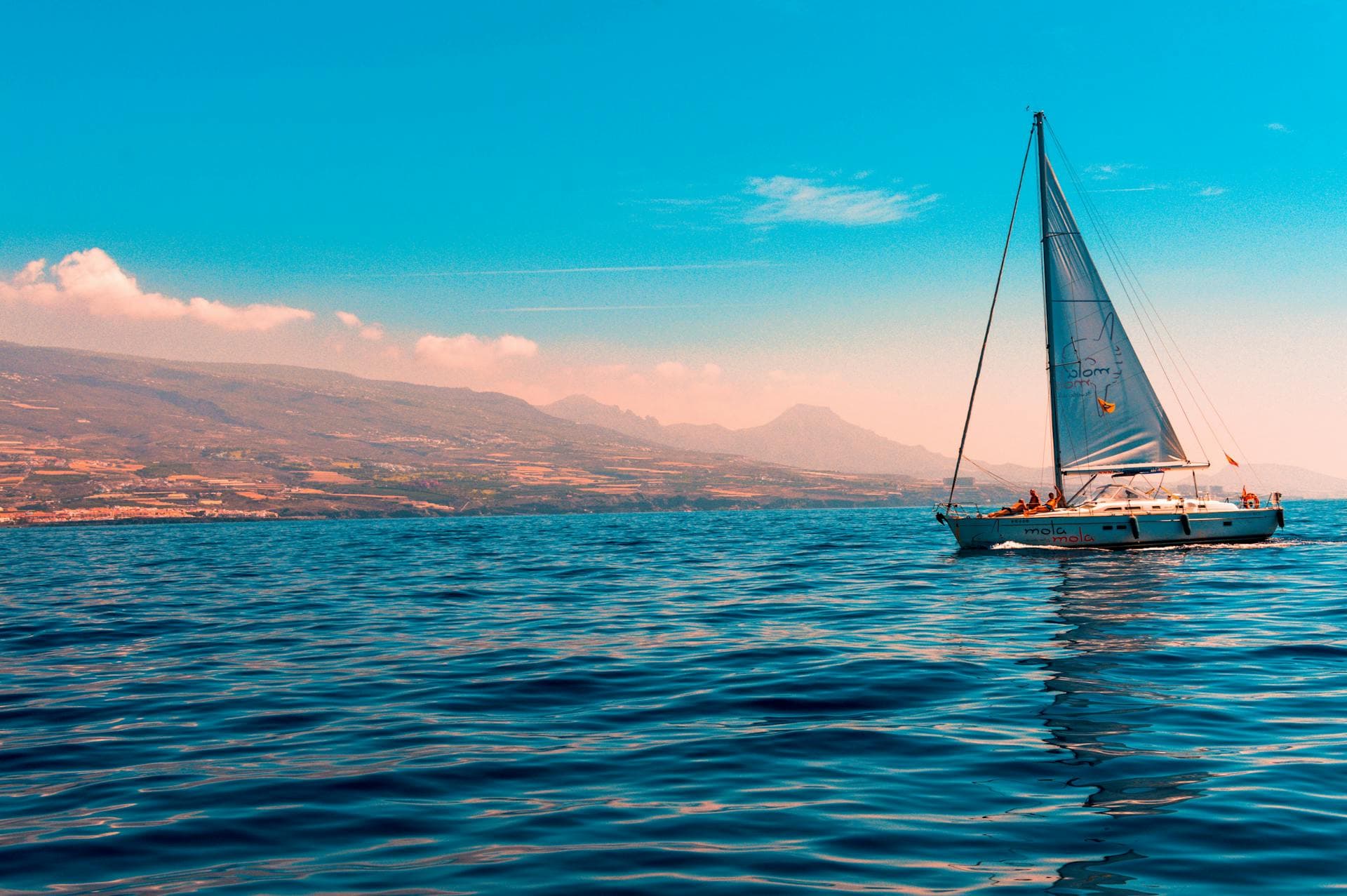 Sailing yacht underway along a temperate, mountainous coast